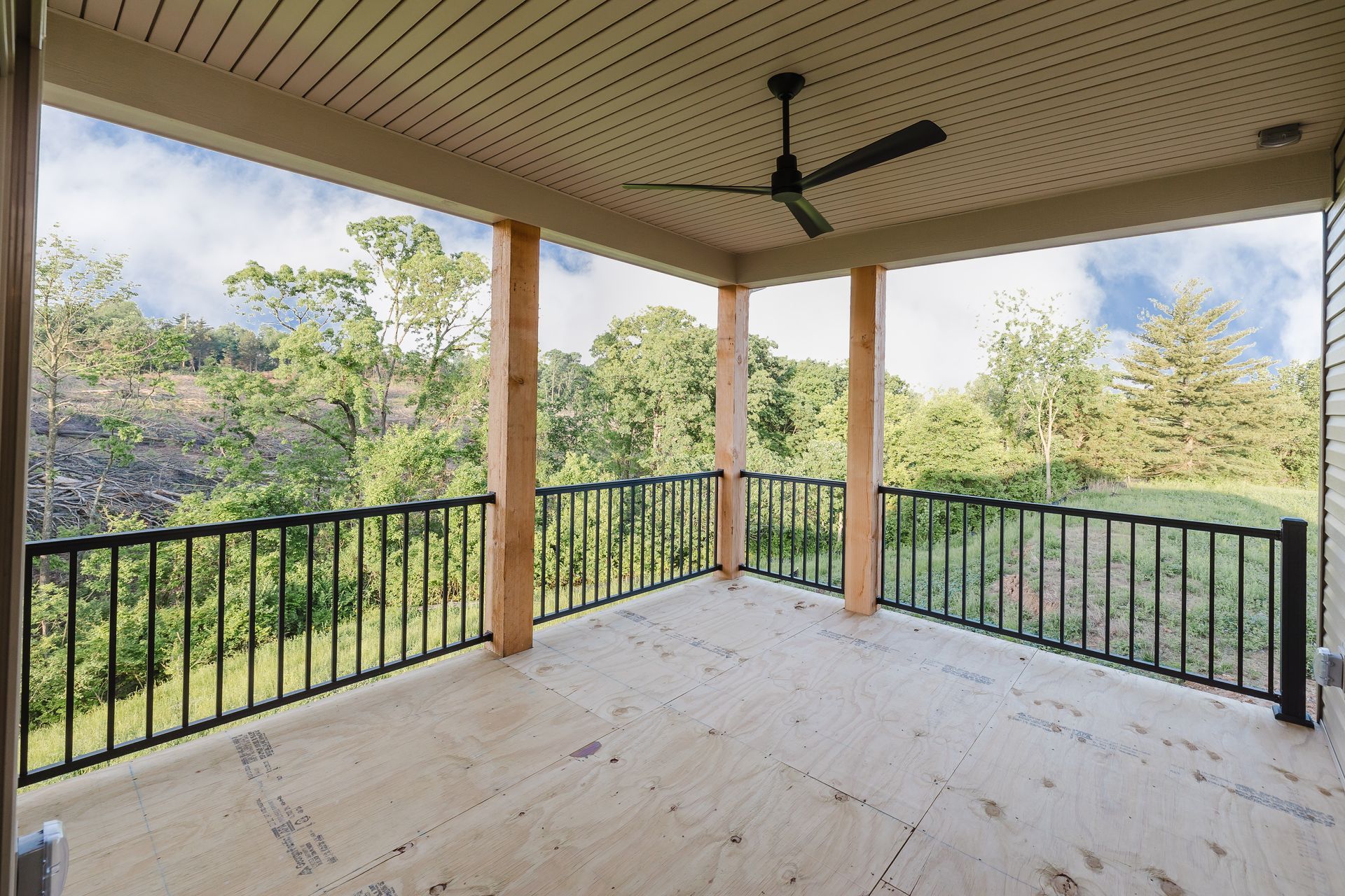 Covered porch of the Dean Martin model with black railing and ceiling fan, overlooking a green, tree-filled landscape.