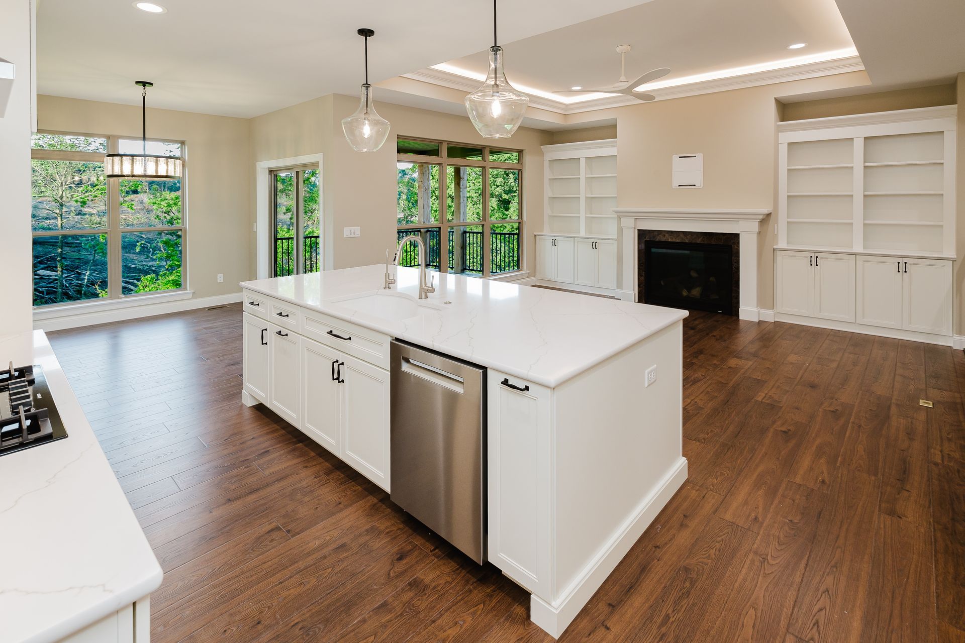 White kitchen of the Dean Martin model with large island, stainless steel appliances, dark wood floors, and bright windows.