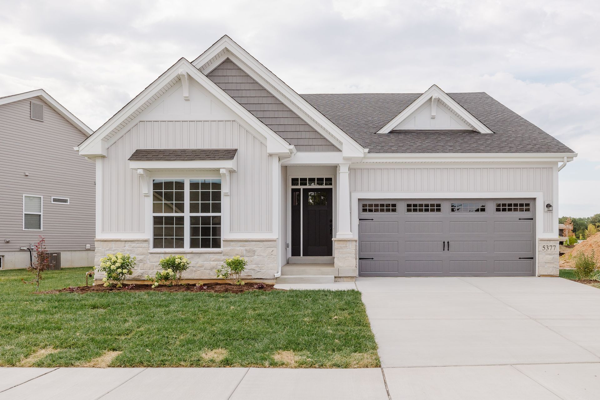 The Cary Grant exterior with gray roof and garage door, light stone accents, and green lawn.