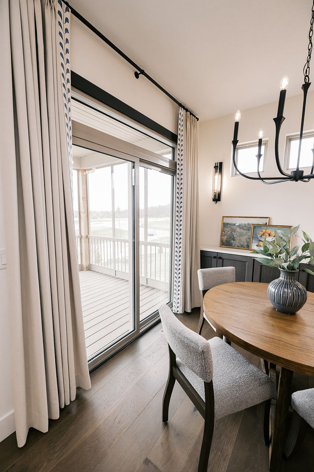 Dining room in the Cary Grant model with a round wooden table, chairs, and sliding door to a balcony, cream curtains.