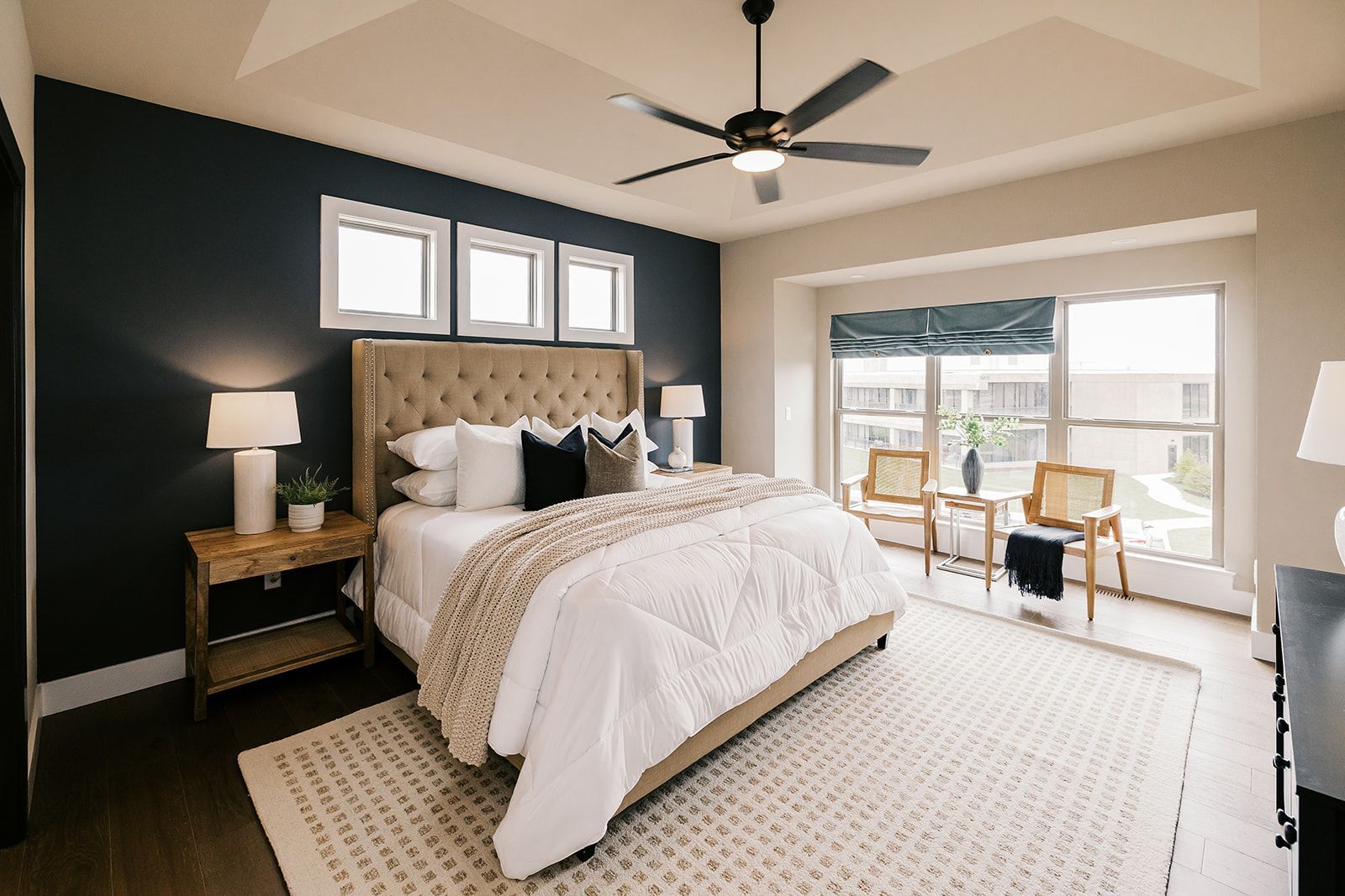 Bedroom in the Cary Grant model  with bed, rug, dark accent wall, and sitting area by a large window.