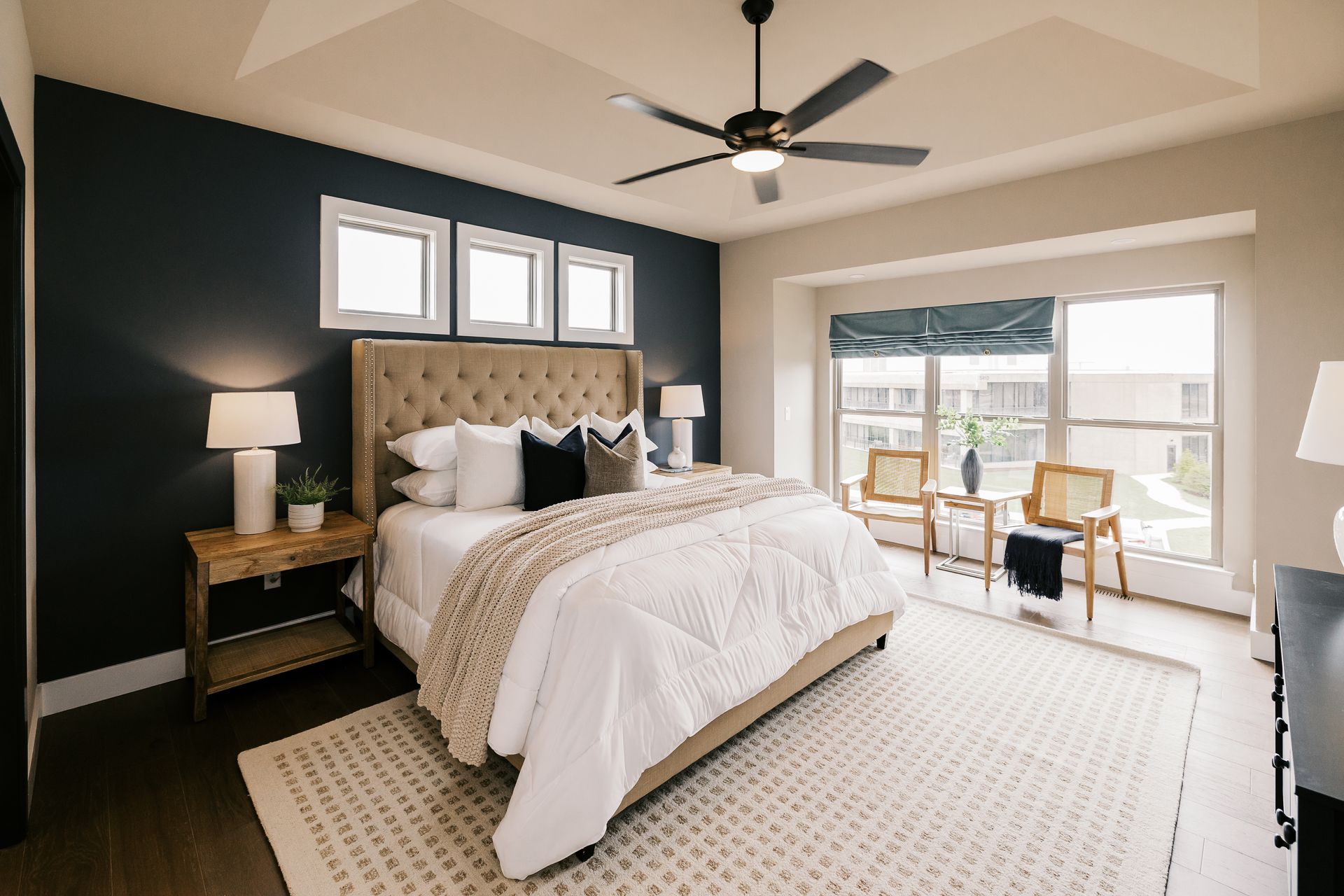 Bedroom in the Cary Grant model with dark blue accent wall, neutral bed, and sitting area with natural light.