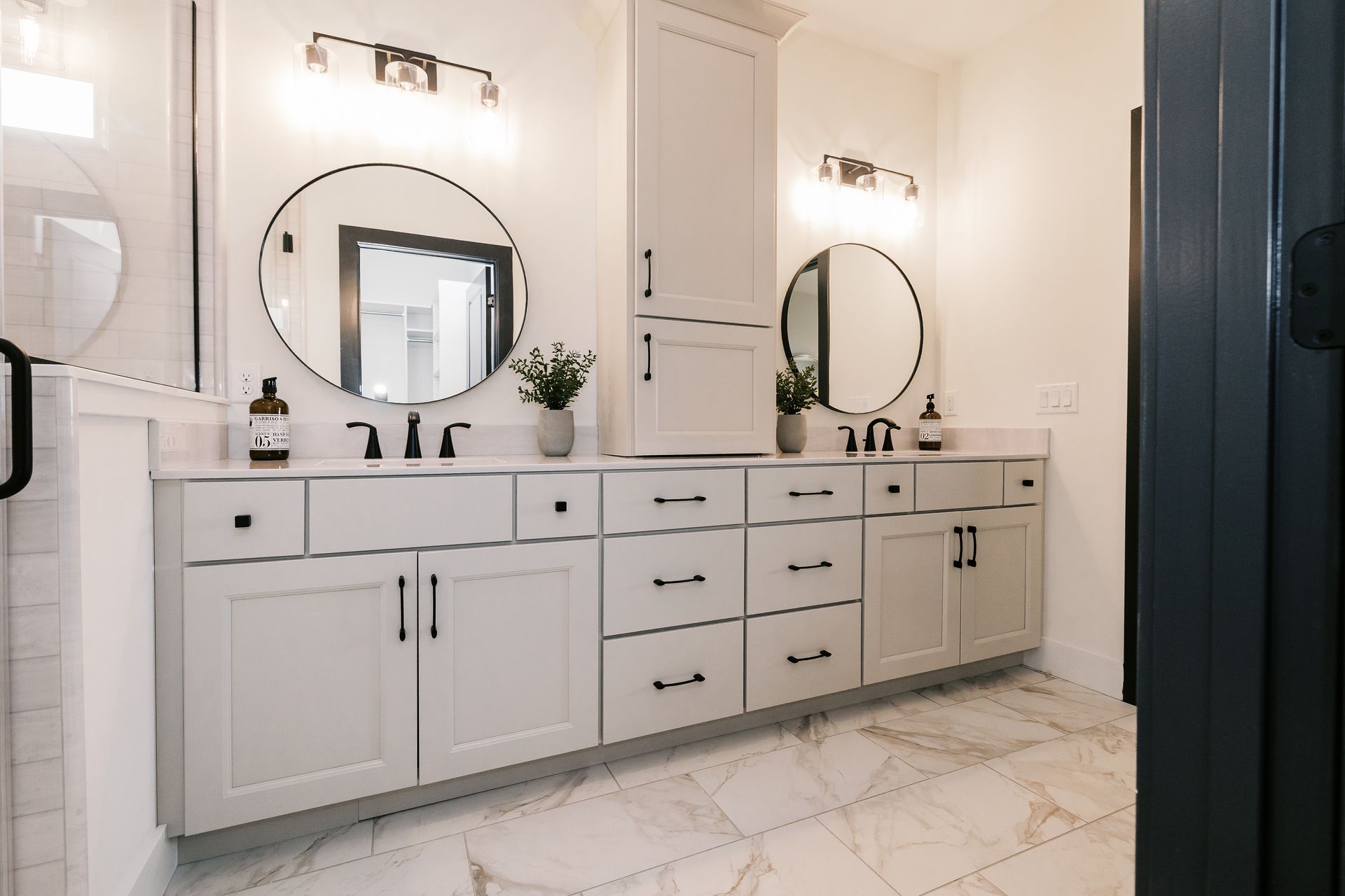 Bathroom in the Cary Grant model with white cabinets, round mirrors, and marble tile flooring.
