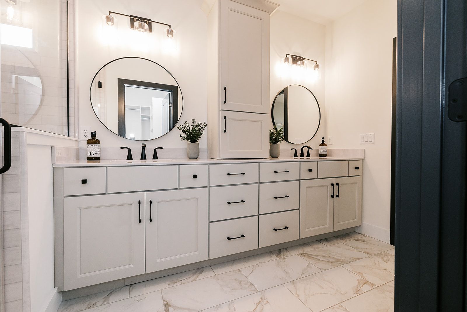 Modern bathroom in the Cary Grant model with white vanity, marble floor, round mirrors, and black hardware.