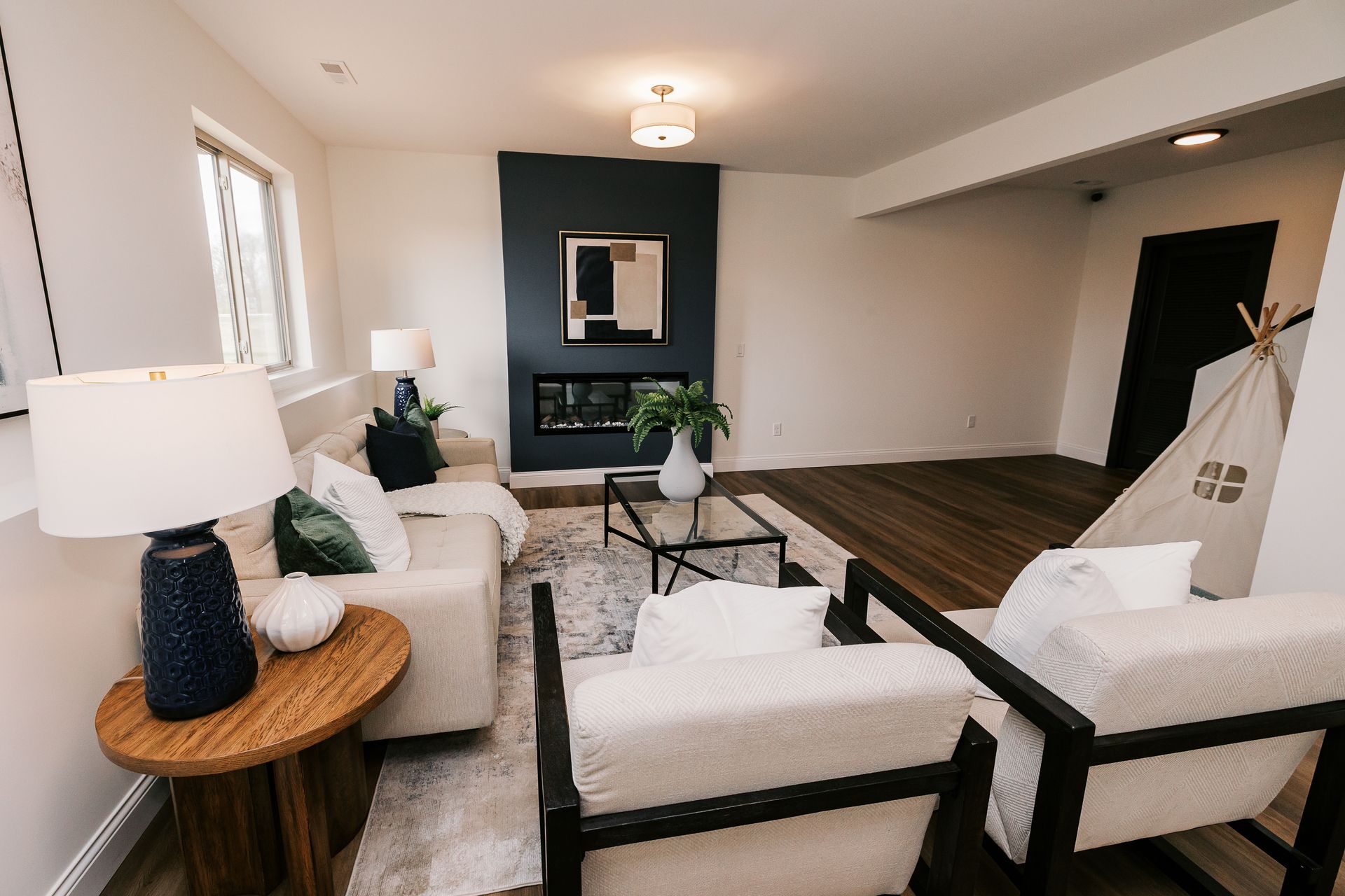 Living room in the Cary Grant model with fireplace, white sofa, armchairs, dark accent wall, and wood floors.