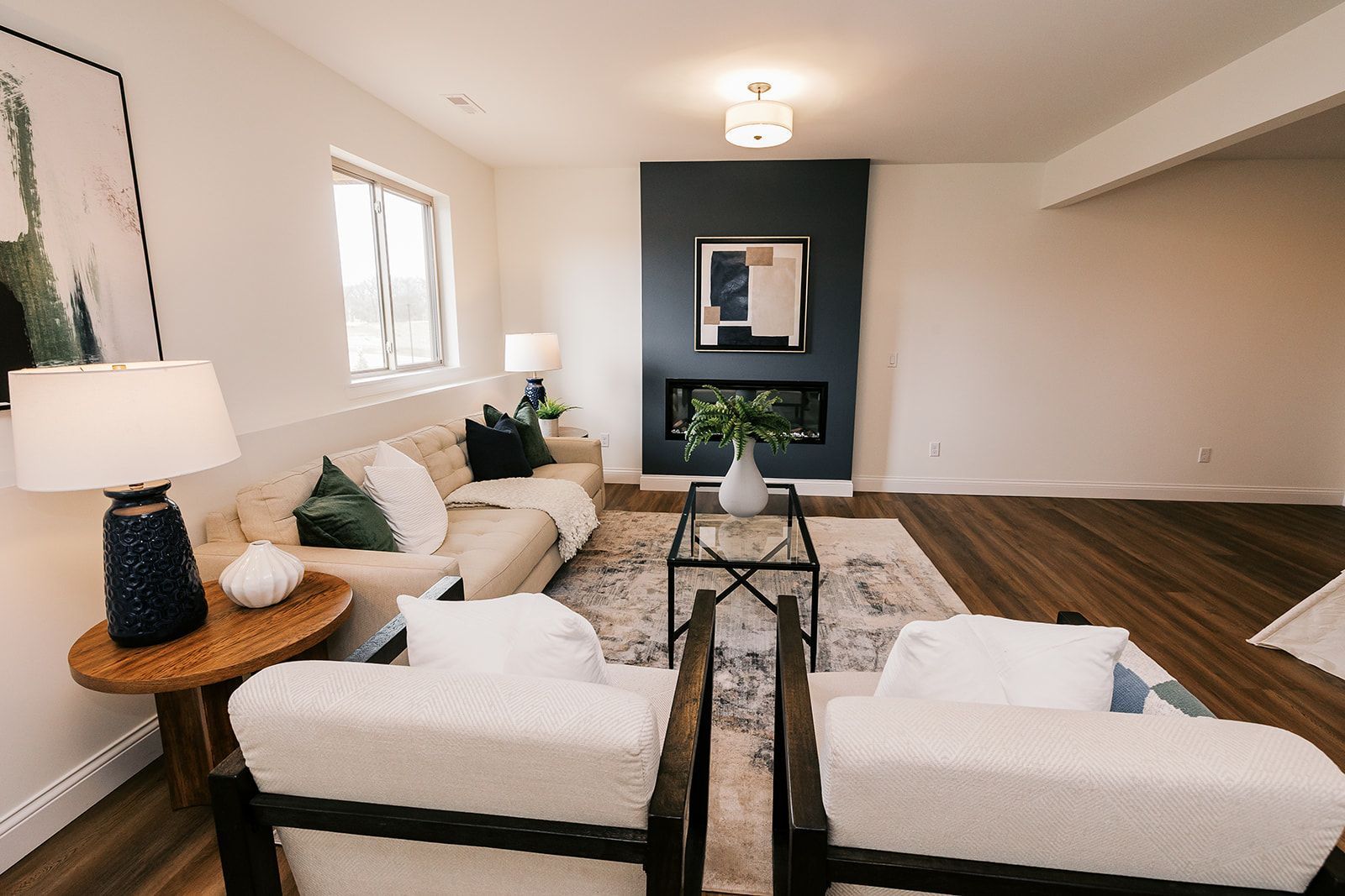 Living room in the Cary Grant model with white walls, dark fireplace, beige sofa, and two white armchairs.