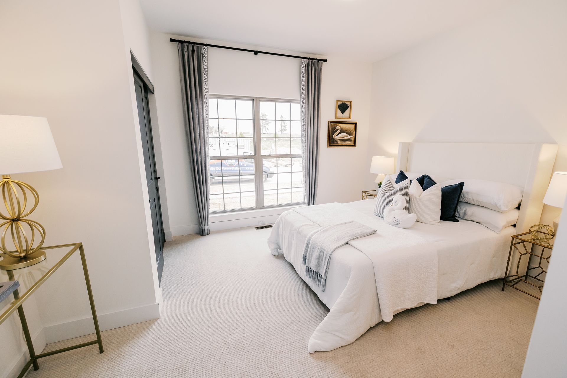 Bedroom in the Cary Grant model with a large white bed, window with gray curtains, and two gold side tables.
