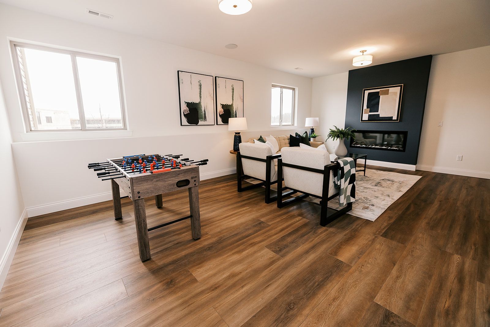 A finished basement at The enclave at Tesson Ridge with a foosball table, seating area, fireplace, and wood floors.