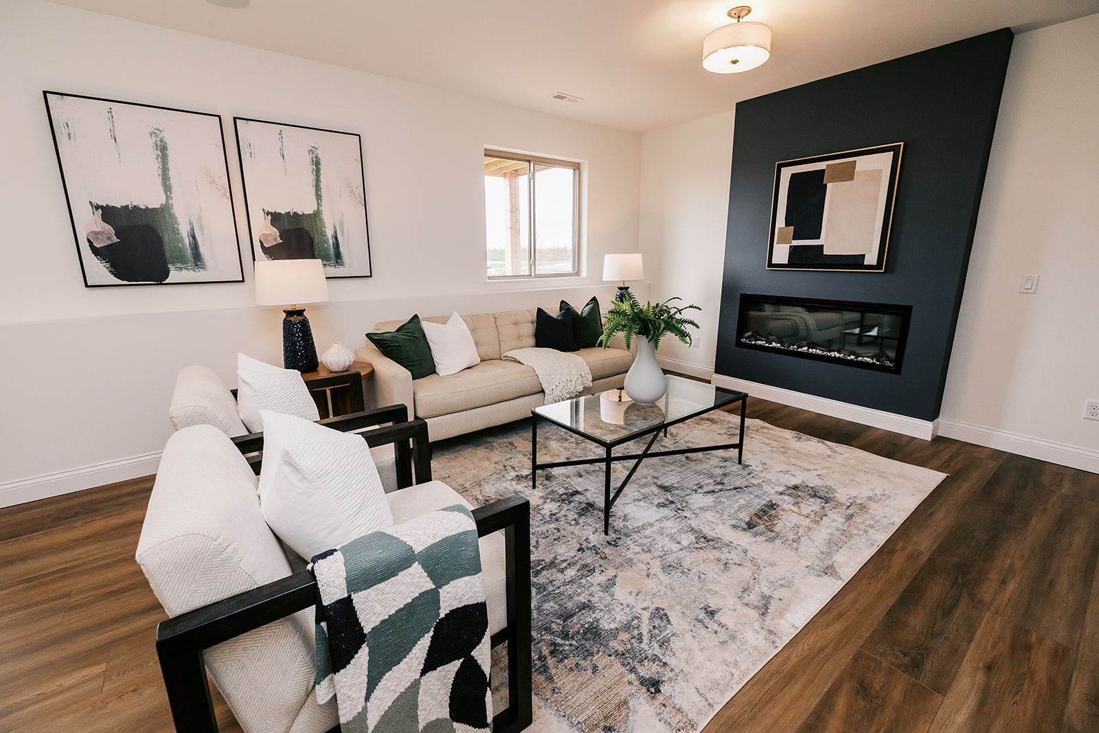 Living room in the Cary Grant model with fireplace, white walls, and wood flooring. Beige sofa, black chairs, and modern art.