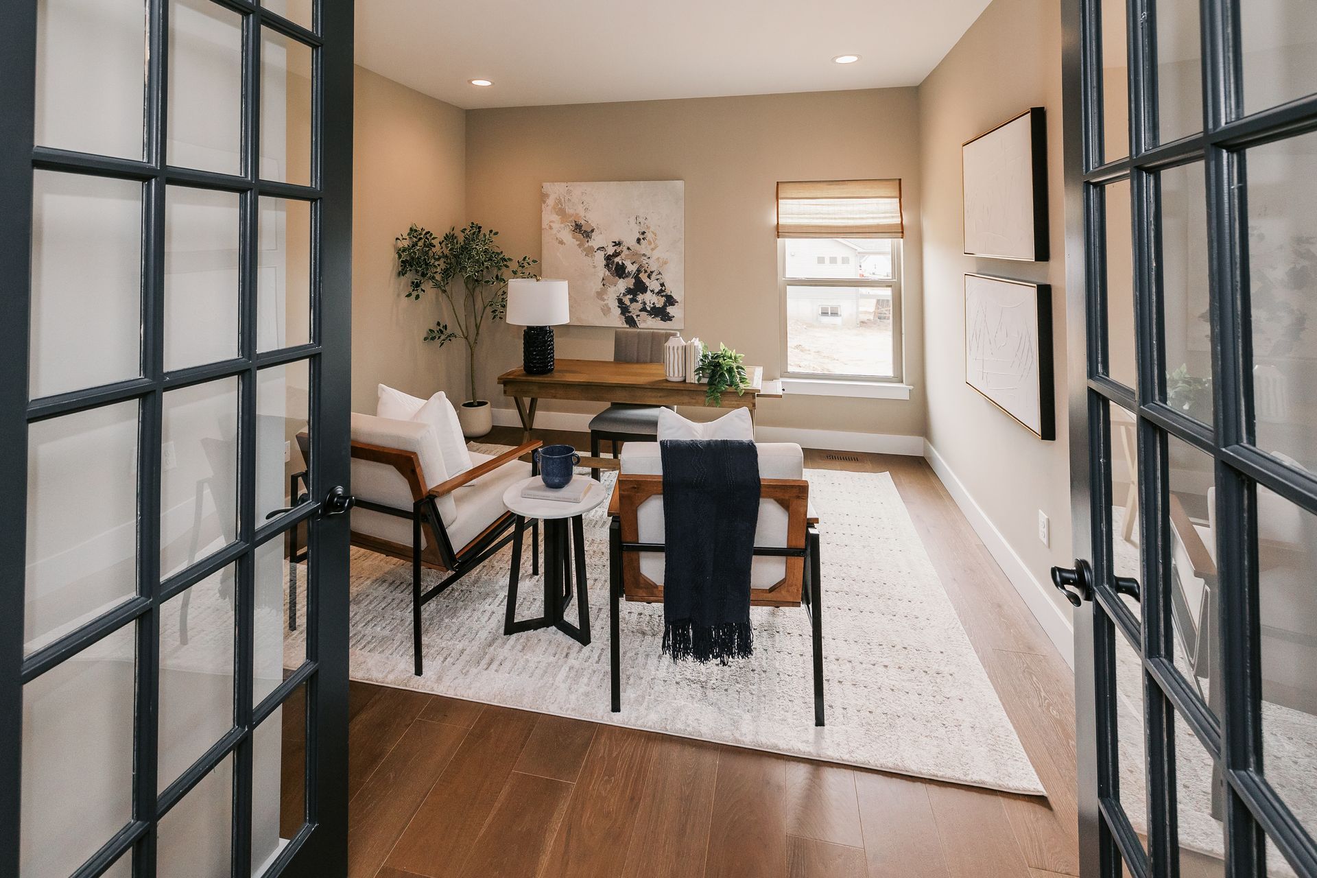 Home office in the Cary Grant model with French doors, desk, chairs, rug, and artwork. Warm neutral tones and natural light.
