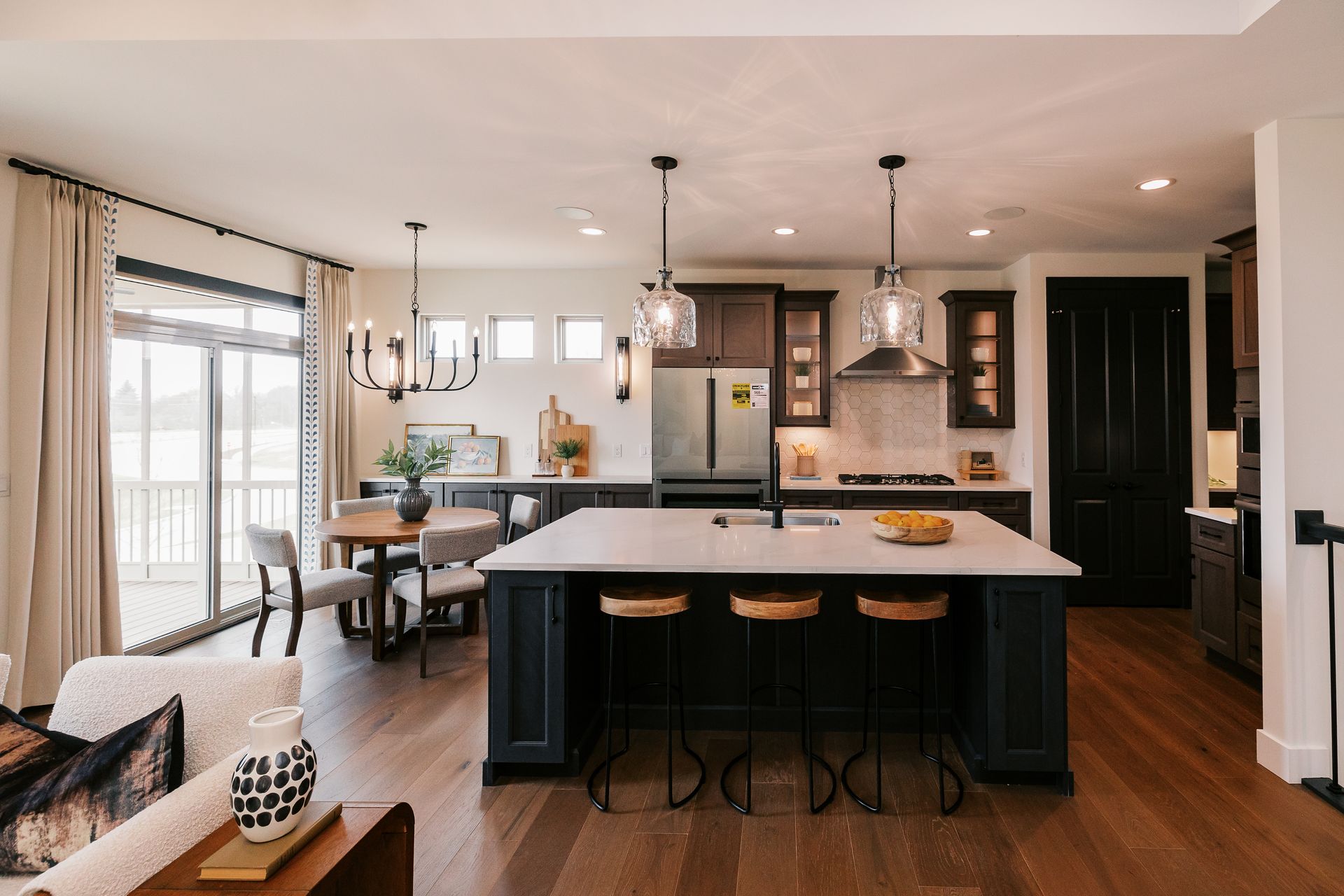 Modern kitchen in the Cary Grant model with dark cabinetry, large island, and dining area next to sliding glass doors.