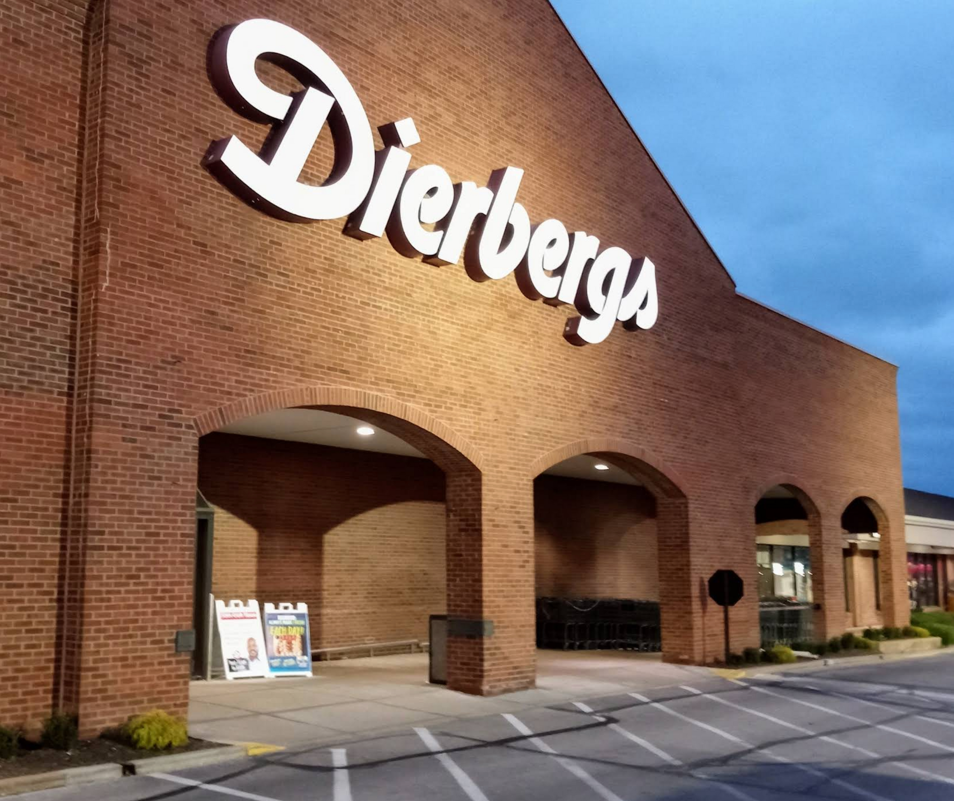 Dierbergs grocery store entrance with arched entryways under a large white sign. Brick facade, dusk setting.