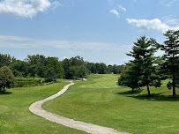 A winding path through a green golf course under a blue sky, trees on the right and left.
