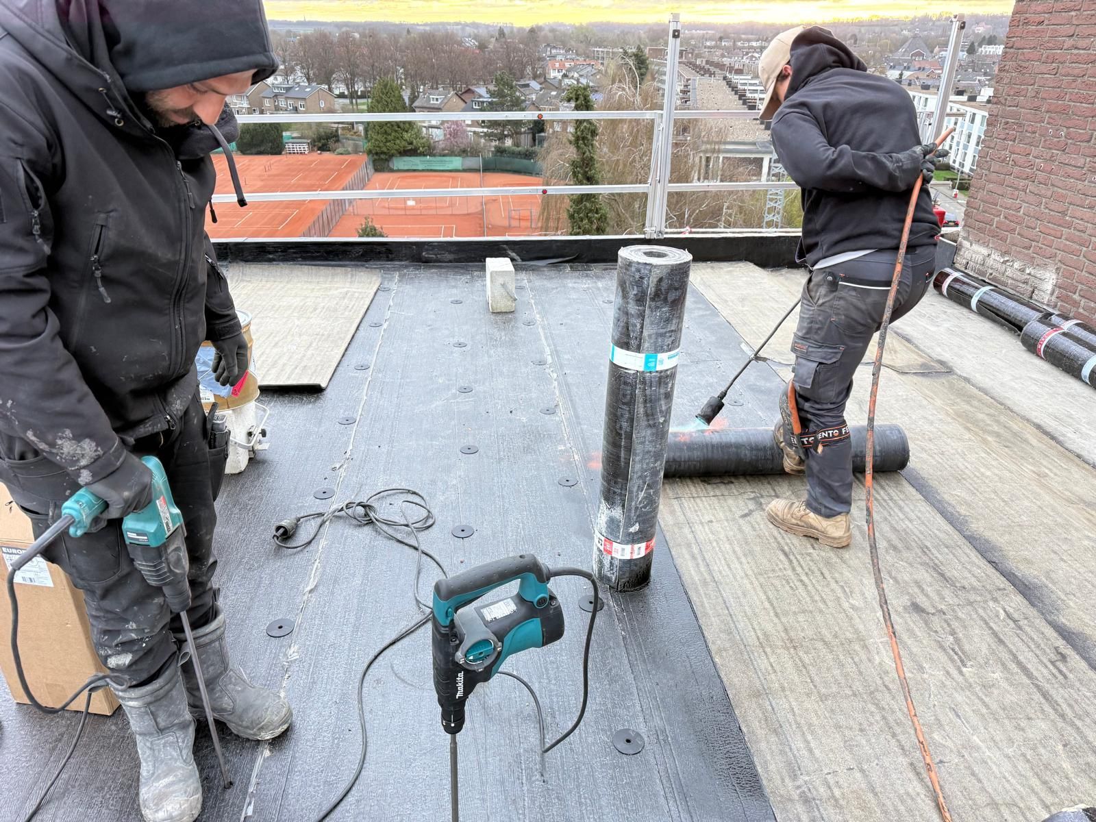 Een arbeider in een feloranje veiligheidsvest loopt langs de rand van een hoog, gegolfd metalen dak tegen een bewolkte hemel.