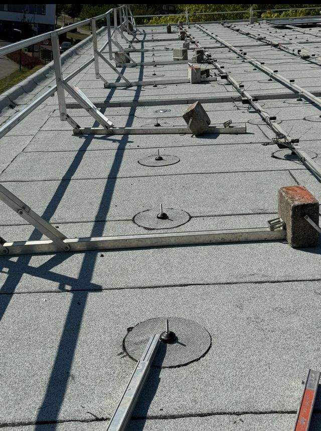 Een plat commercieel dak met een metalen reling en rijen verankeringspunten met ballast, vastgezet met betonblokken.