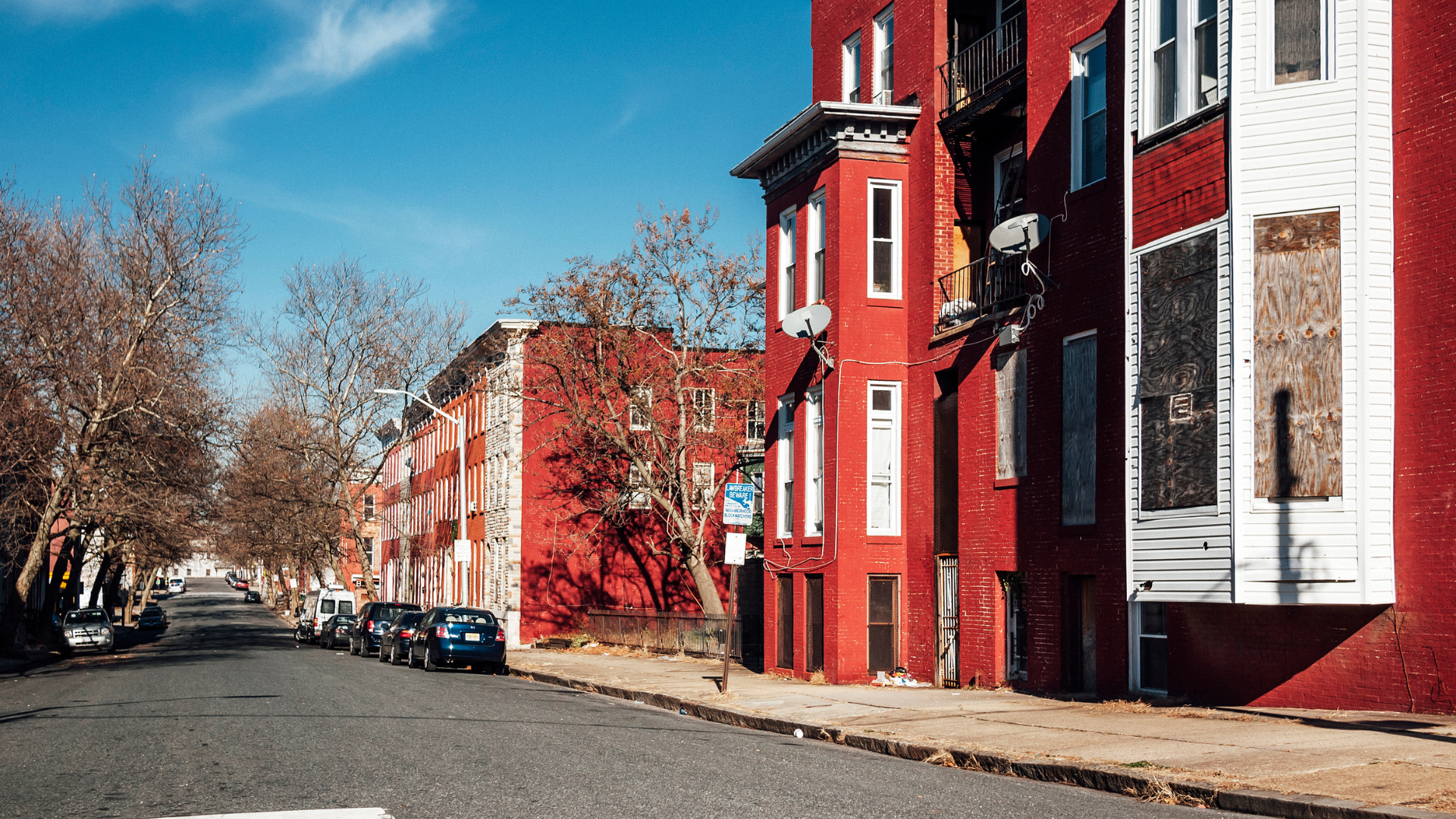 A row of red brick buildings on a city street with cars parked on the side of the road.