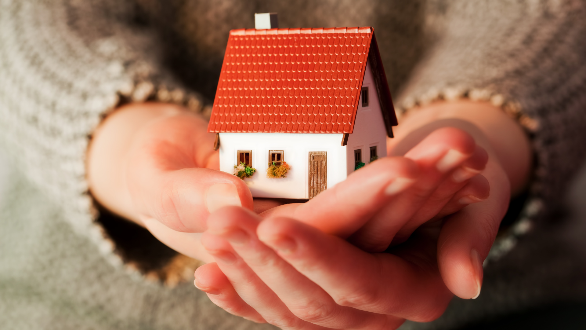 A person is holding a small house in their hands.