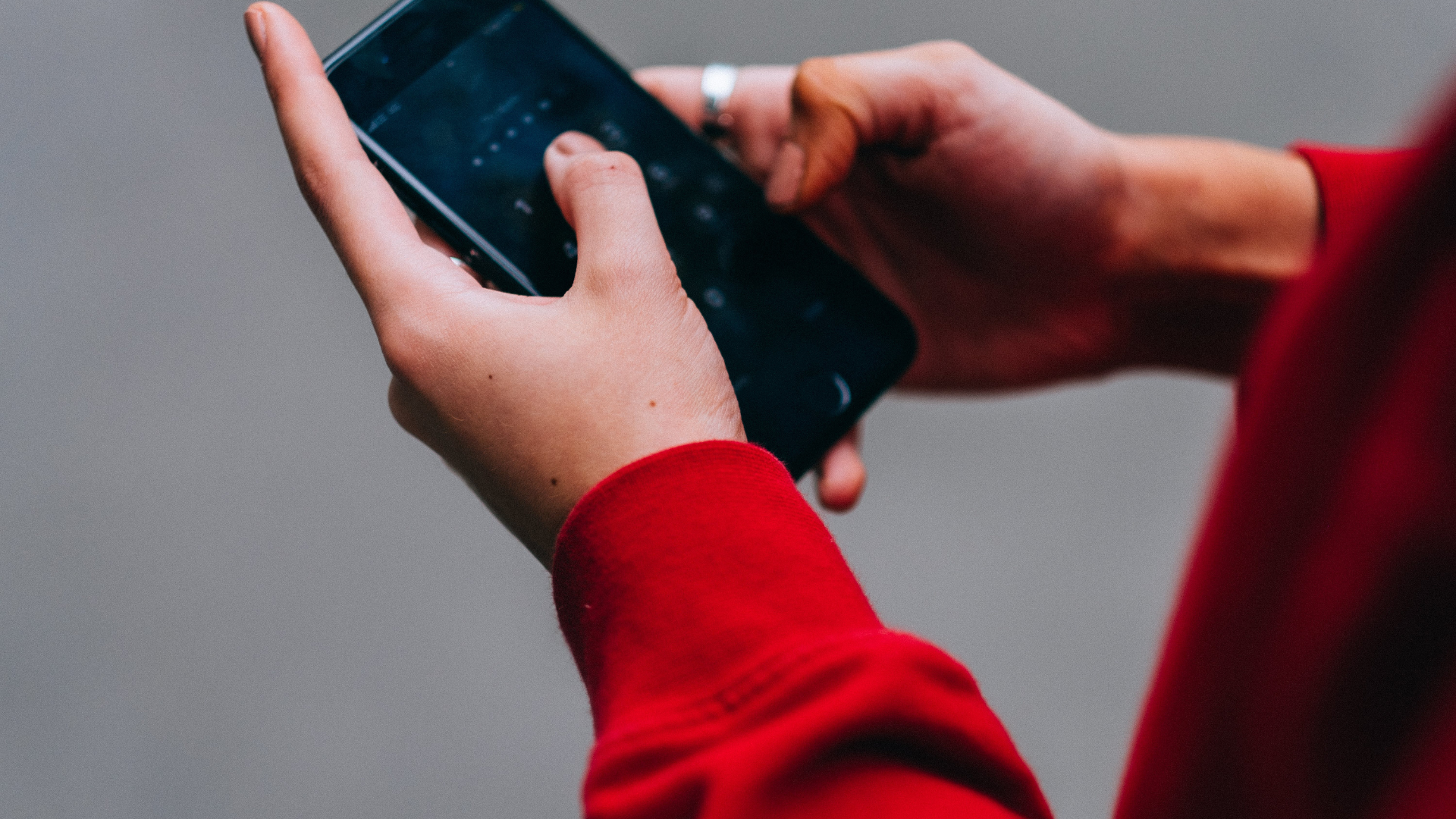 A person in a red sweater is holding a cell phone in their hand.