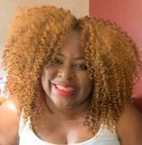 A woman with curly hair is smiling and wearing a white tank top.