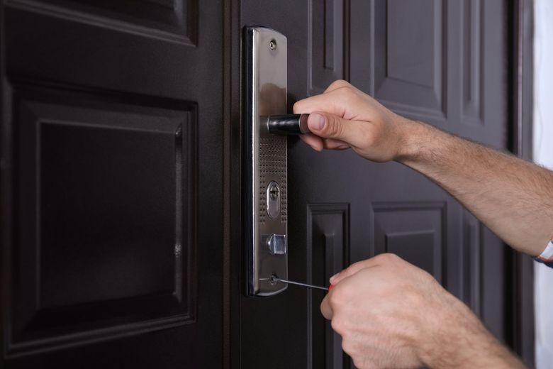 Hands adjusting a silver door lock on a dark paneled front door
