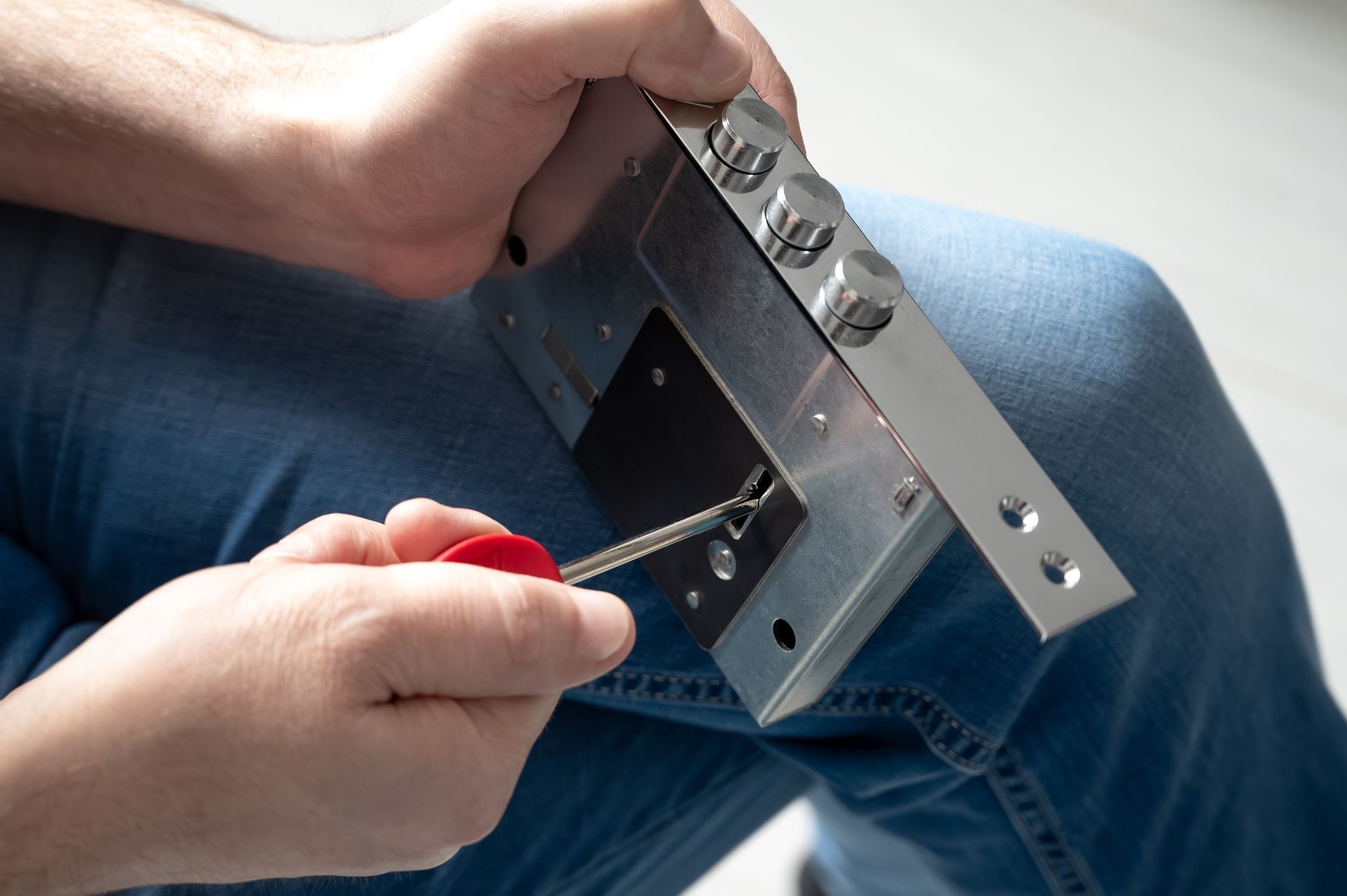 Hands using a screwdriver to adjust a metal electronic device on a lap with blue jeans.