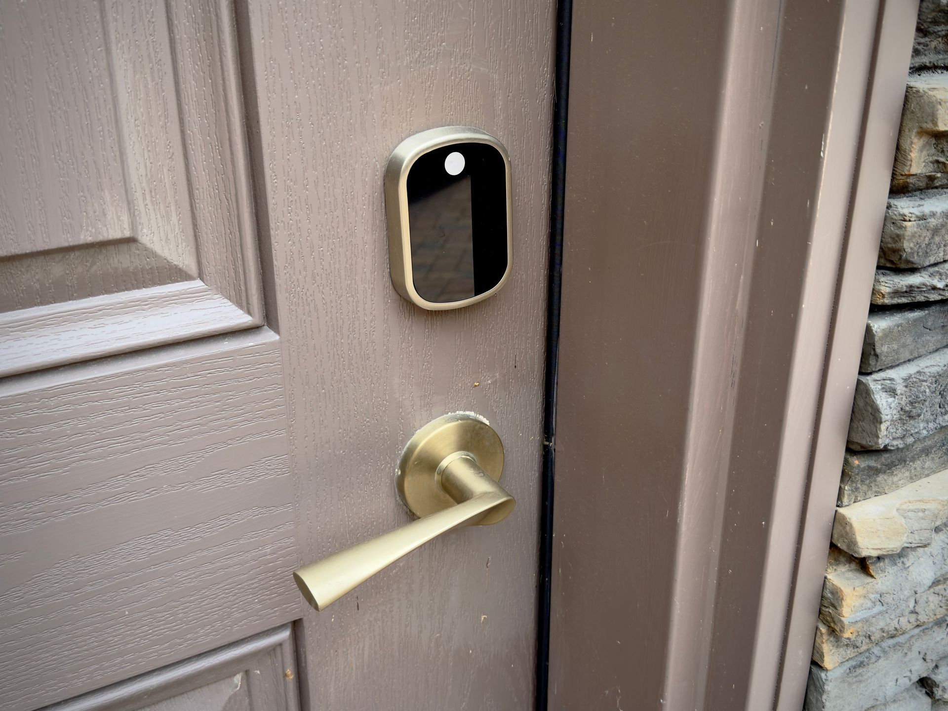 Front door with a black video doorbell and brass handle on a brown exterior door