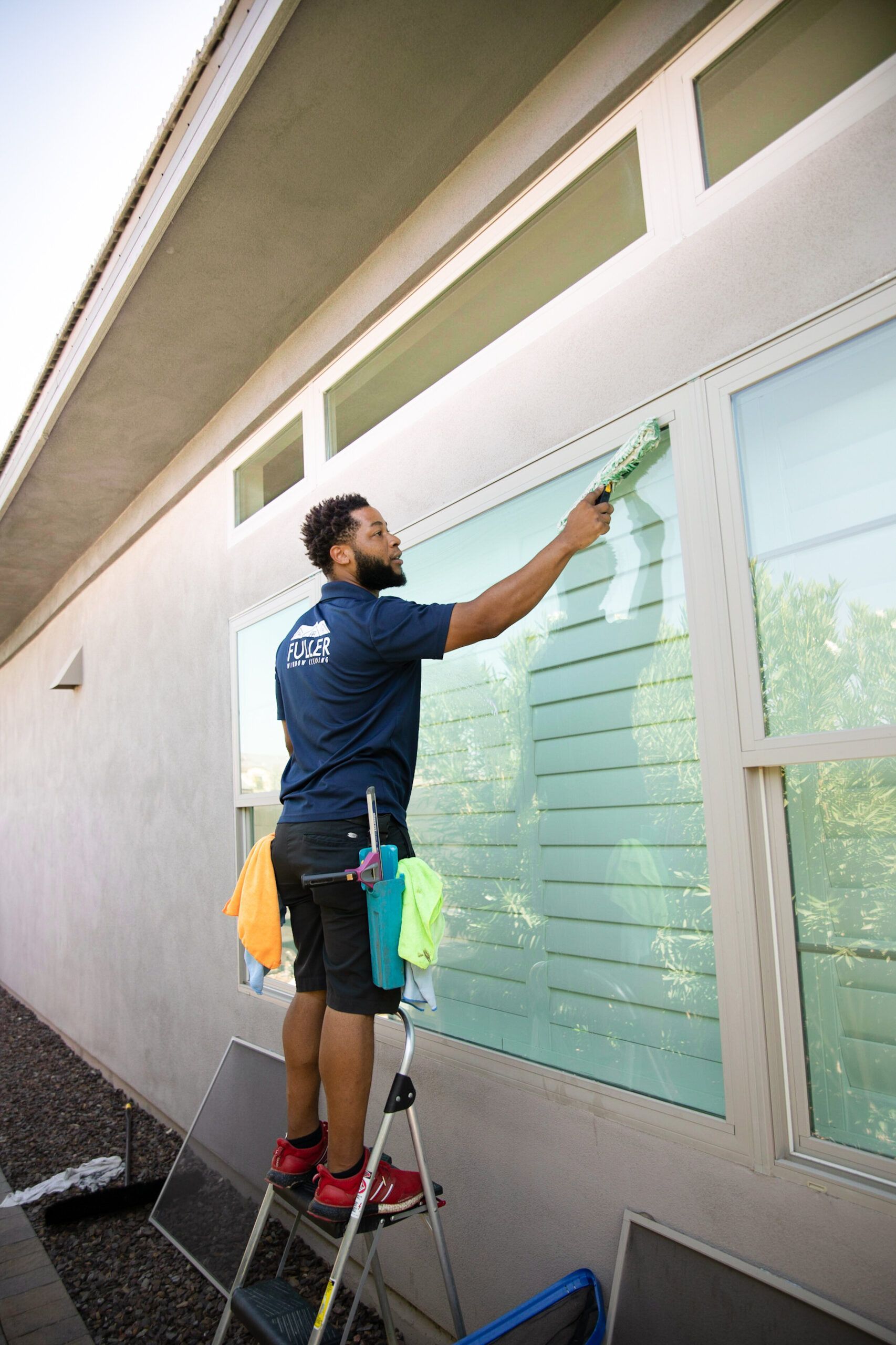 Worker on a ladder painting exterior windows of a building with a roller