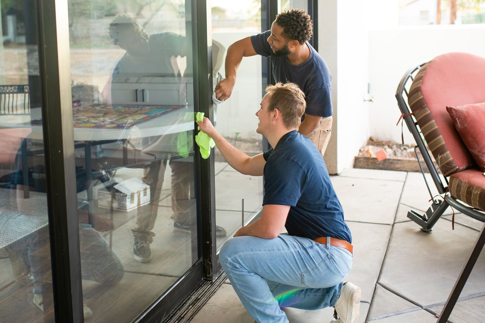 Two people cleaning a glass door with green cloths in a bright room