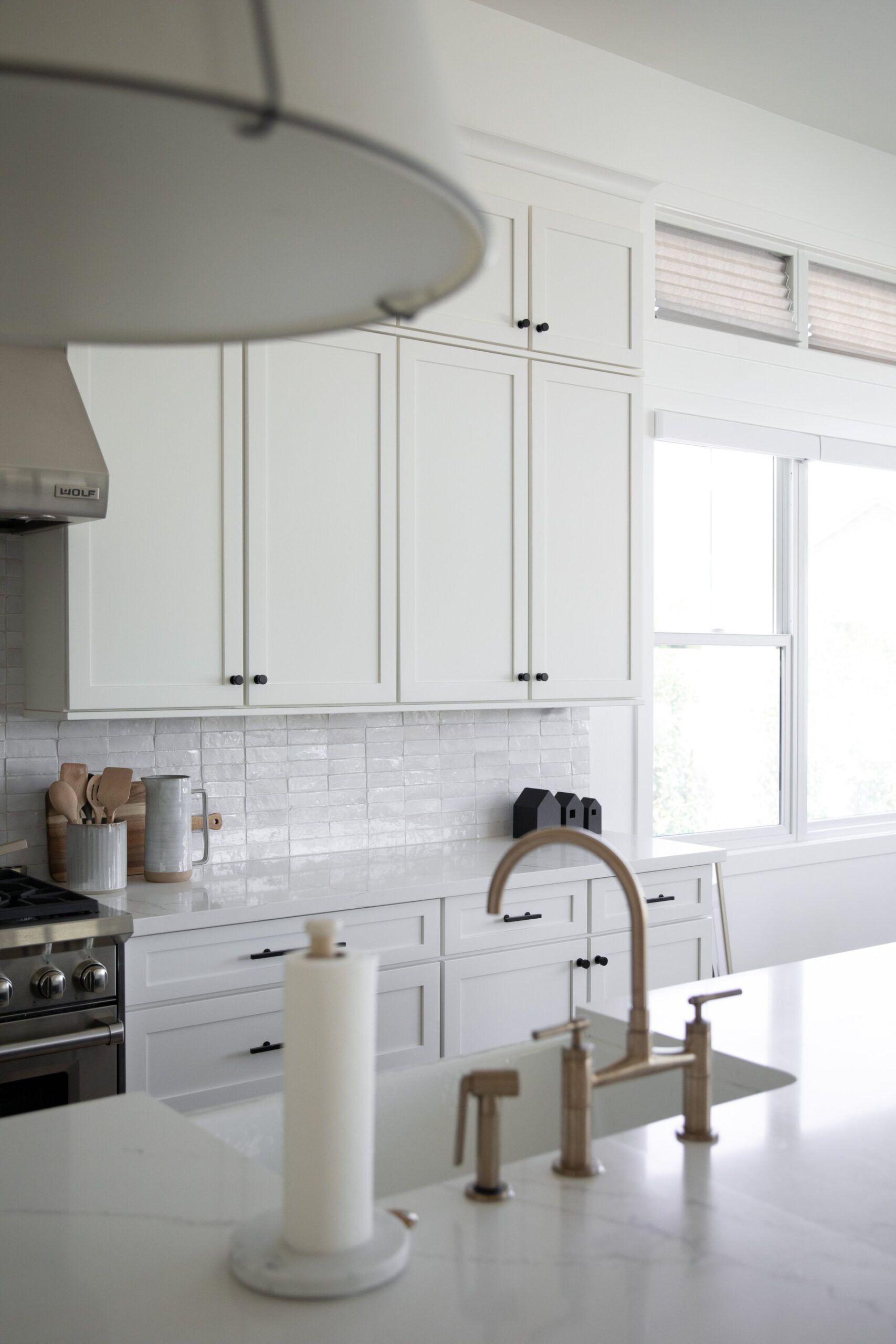 Bright modern kitchen with white cabinets, marble island, and brass faucet by a window