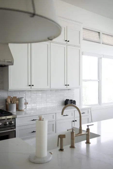 Bright white kitchen with cabinets, stove, window, and island sink faucet