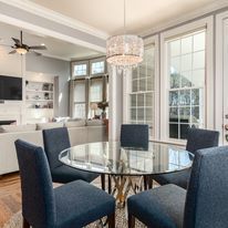 Elegant dining room with glass table, navy chairs, crystal chandelier, and French doors to a bright patio