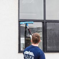 Worker cleaning a window with a blue squeegee on the exterior of a building