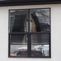 Black-framed window on a light exterior wall reflecting nearby trees and rooflines