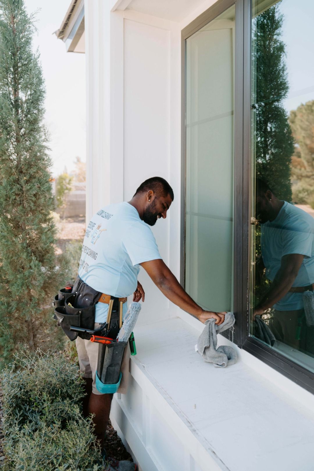 Worker cleaning a white windowsill beside a glass door on a house exterior