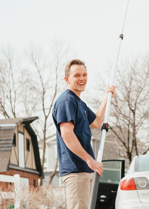 Person holding a long pole and smiling outdoors near parked cars and a house.