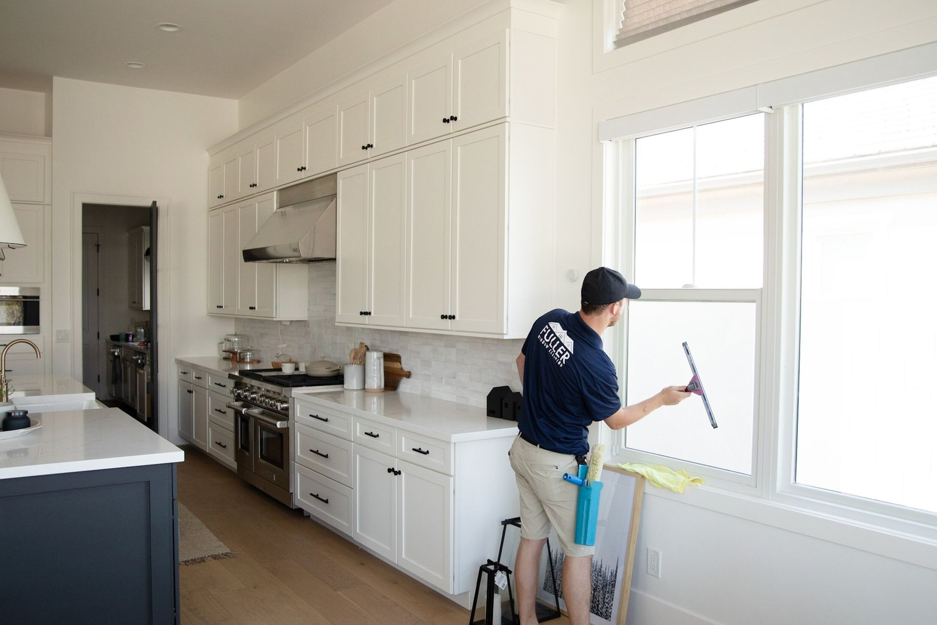 Person painting a white kitchen window frame with a paint roller