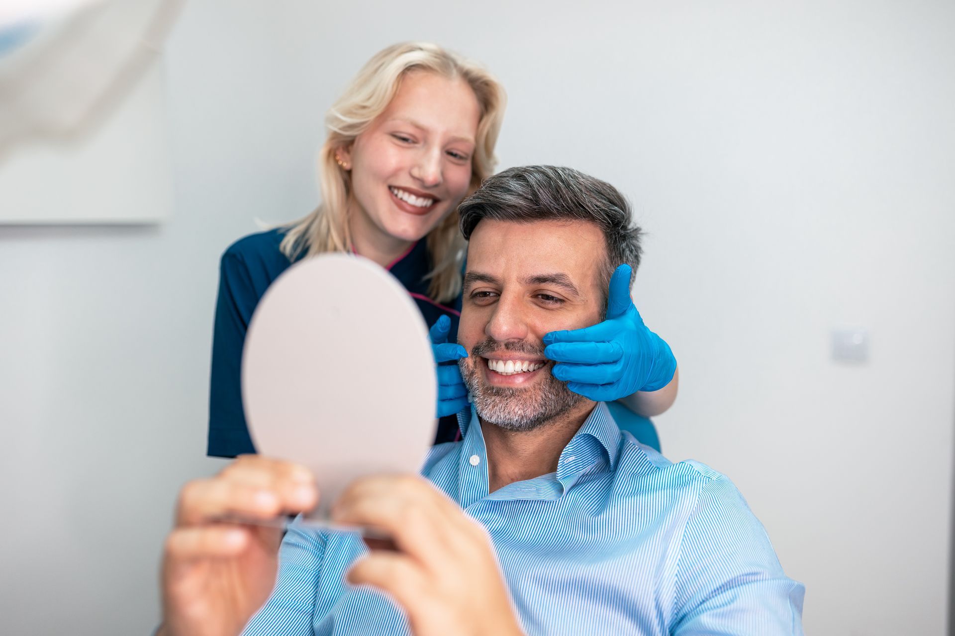 Man smiling at his restorative dentistry results in a handheld mirror.