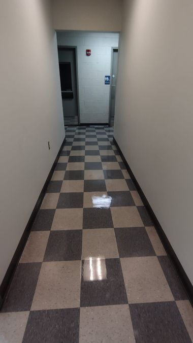 Narrow hallway with checkered tile floor and white walls leading to a doorway.