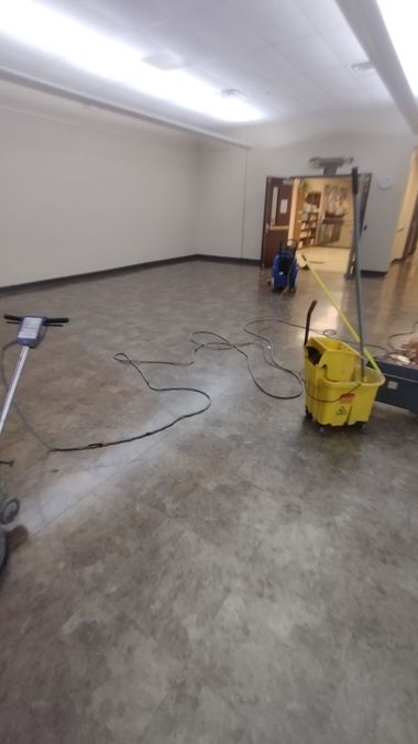 Large empty room with concrete floor, cleaning equipment, and a doorway at the far end.
