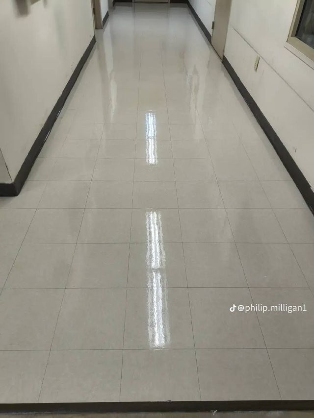 Empty tiled hallway with white walls and bright overhead light reflection on the floor
