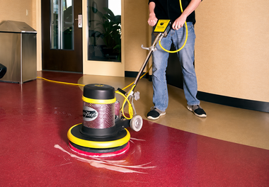 Person using a floor buffer on a glossy red floor in a hallway