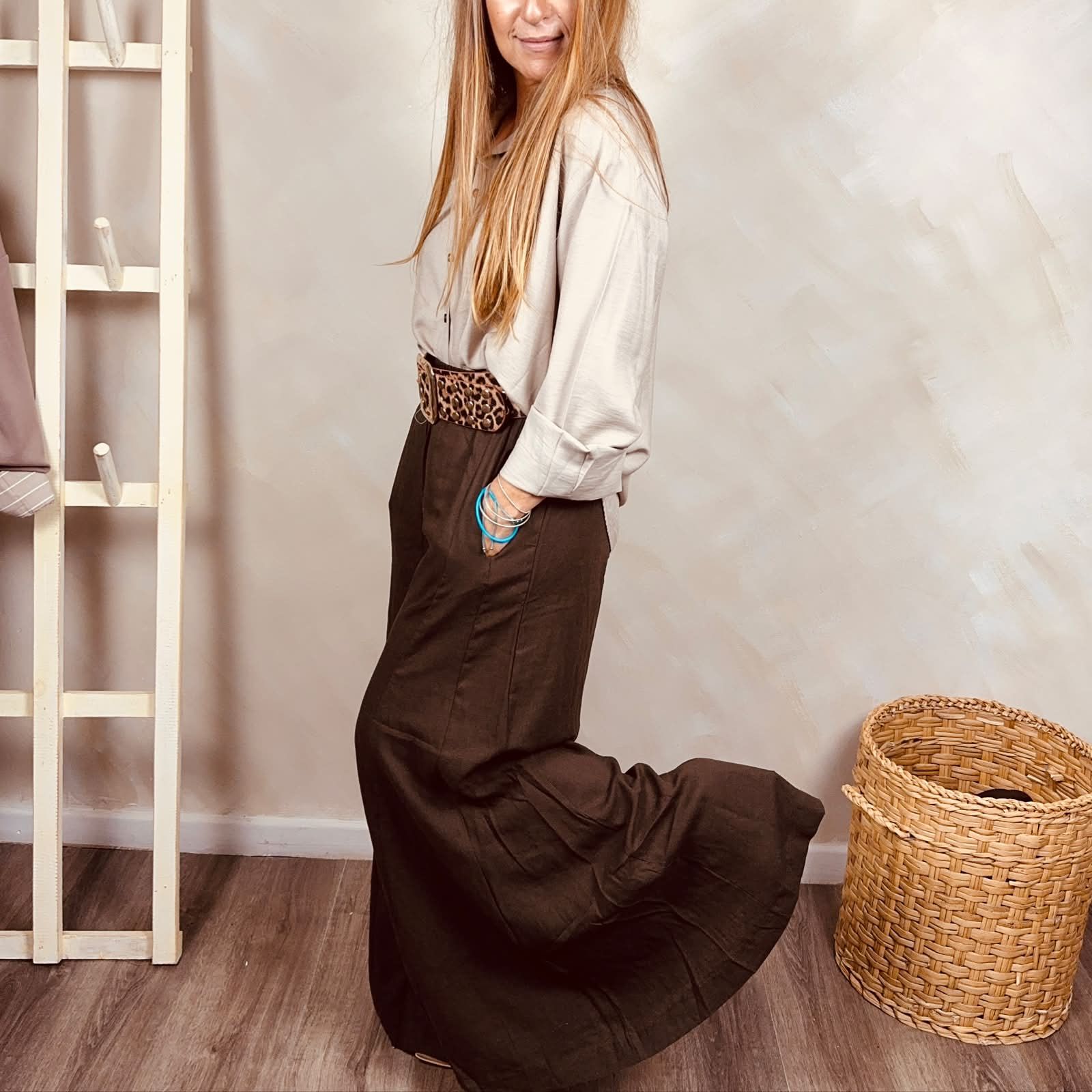 Mujer de pie en el interior de una casa, con blusa color crema y falda marrón oscuro, junto a una cesta de mimbre.