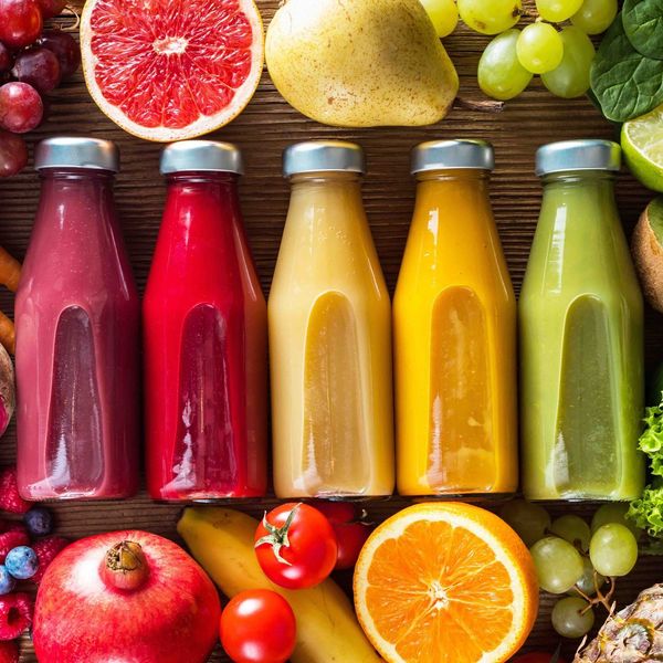 A row of juice bottles surrounded by fruits and vegetables