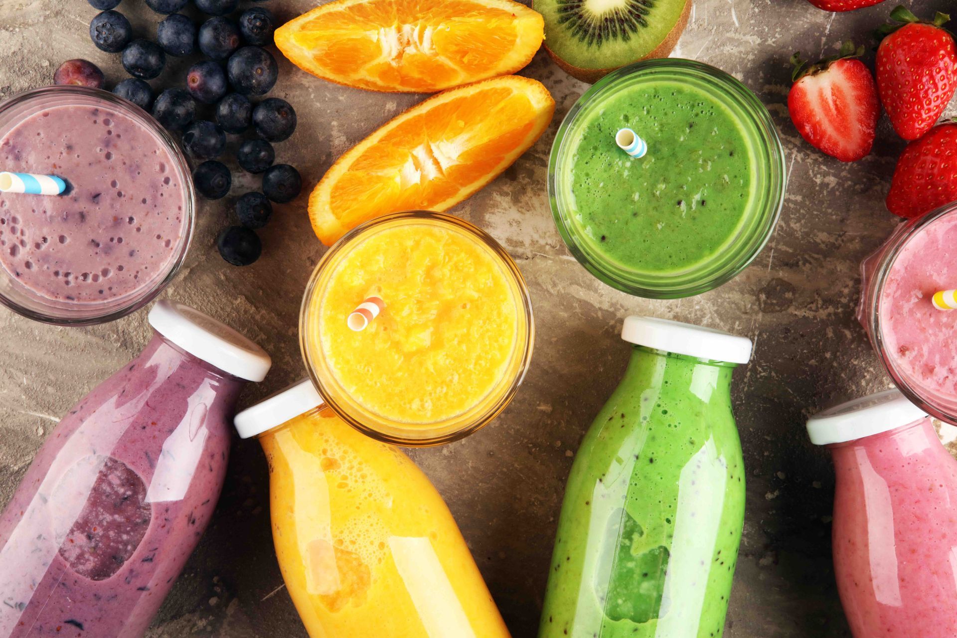 A variety of fruit smoothies in bottles and glasses on a table.