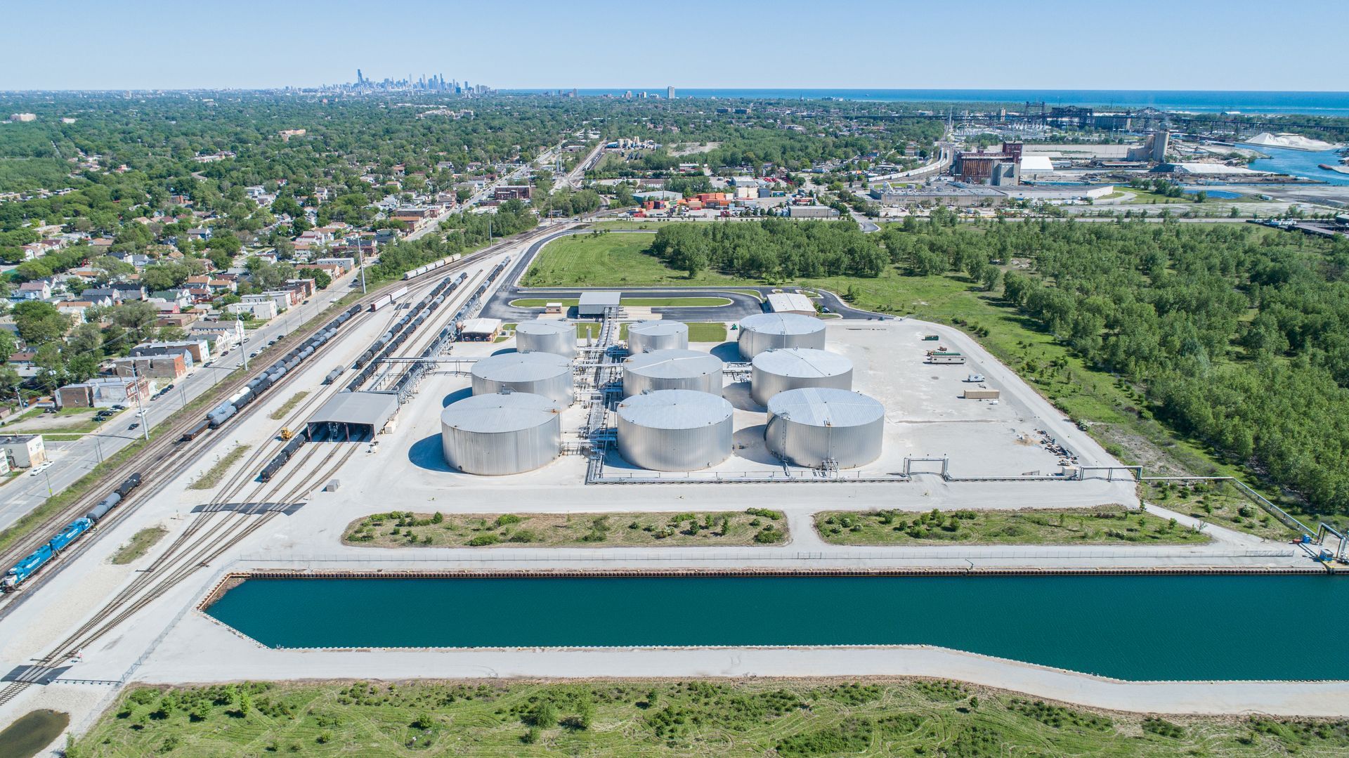 An aerial view of a large oil refinery surrounded by trees and a body of water.