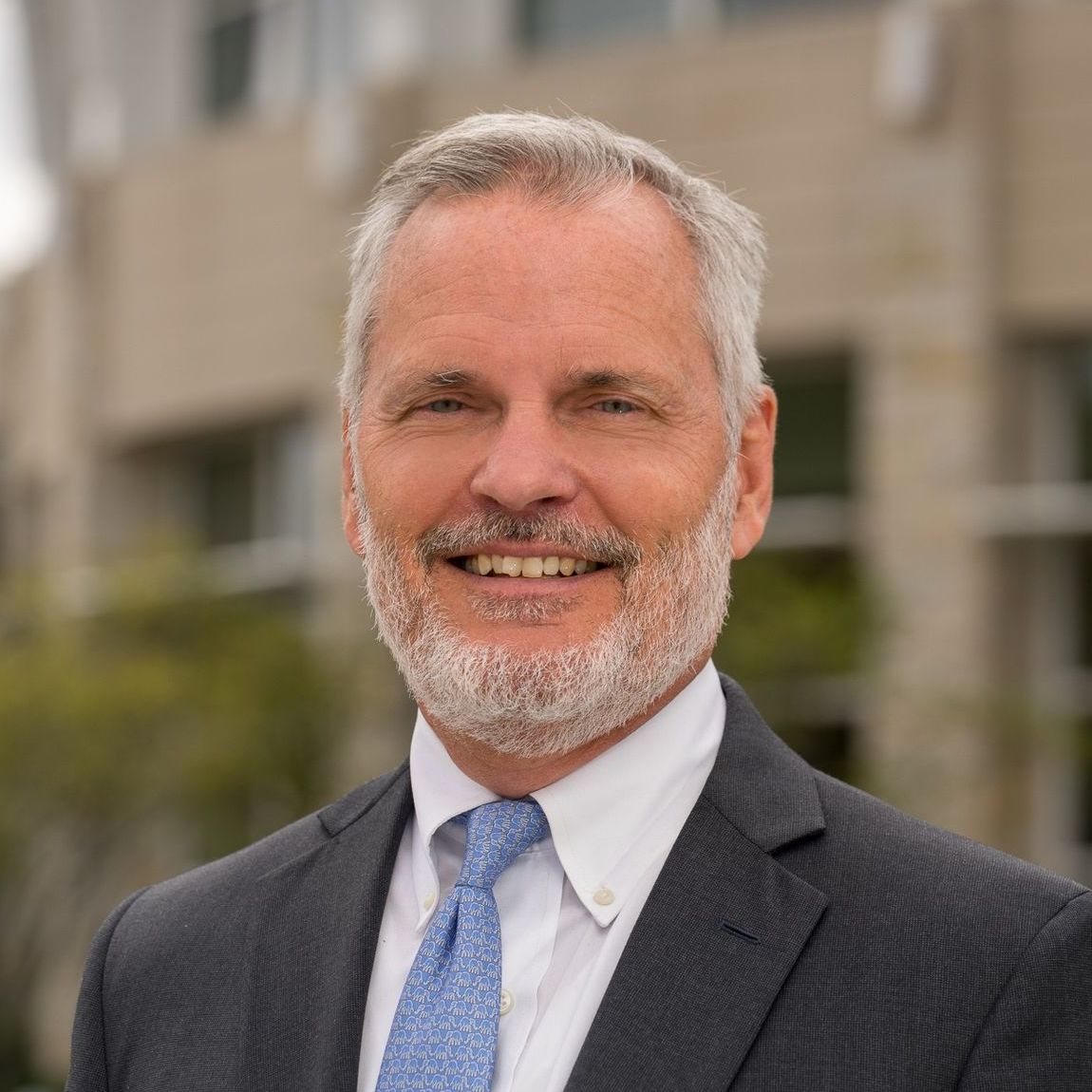 A man in a suit and tie is smiling in front of a building.