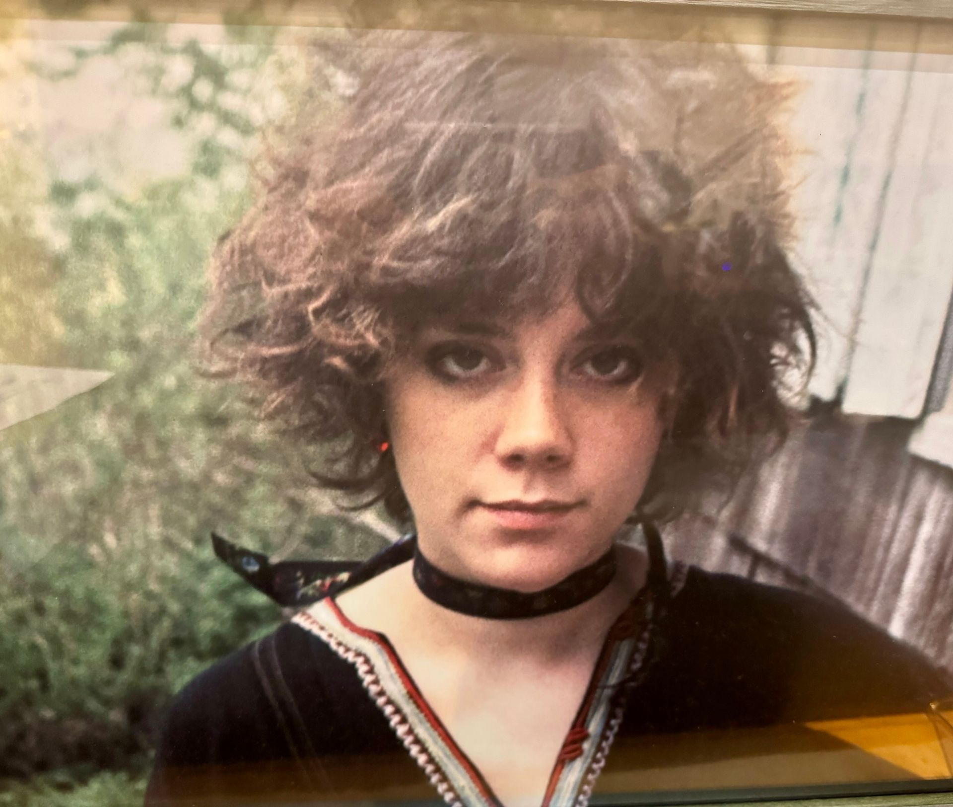 A woman with curly hair is wearing a choker around her neck.