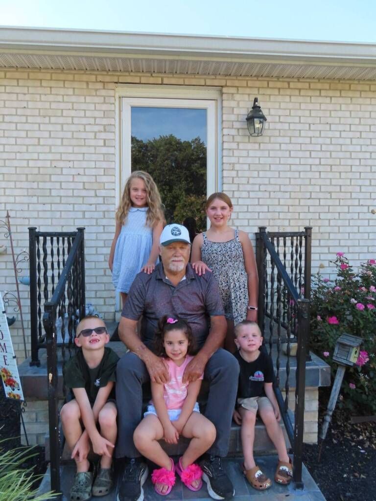 Family posing on front steps of a brick house, with two children sitting in front and others standing behind.