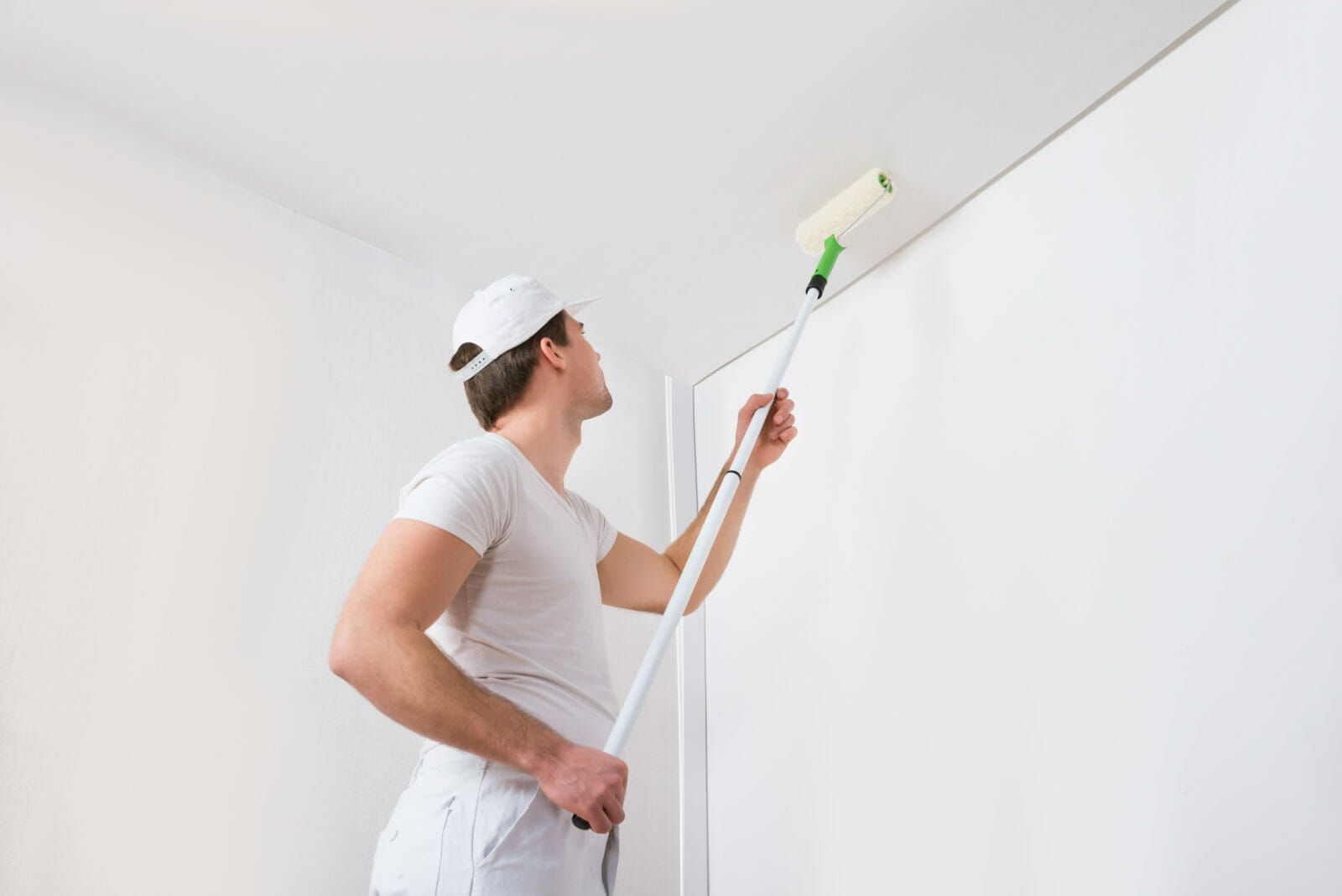 A man is painting the ceiling of a room with a paint roller.