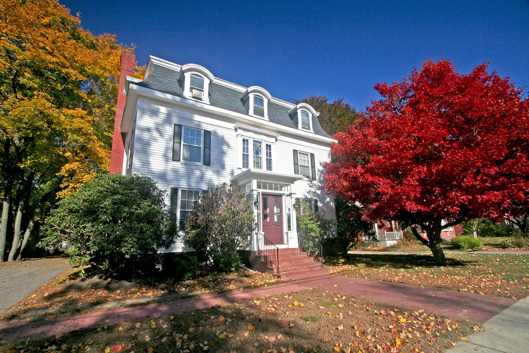 Exterior view of two story white home with red door and trees in front yard.